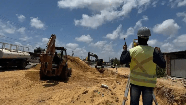 Máquinas trabalham na terraplenagem de avenida em duplicação na Zona Norte de Natal, com operário de colete em primeiro plano.