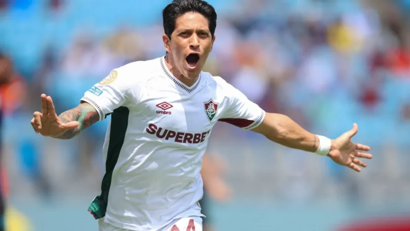 Jogador do Fluminense com uniforme branco comemora com os braços abertos em campo