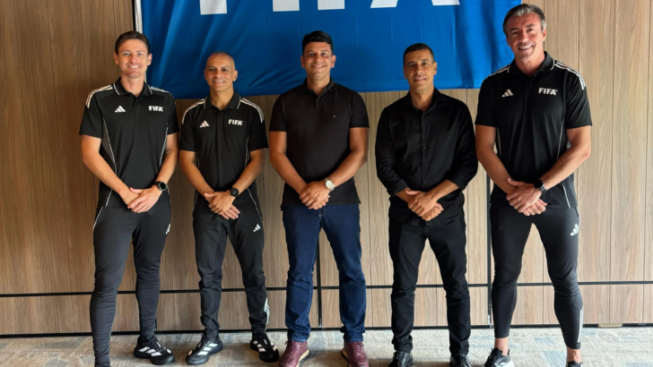 Grupo de árbitros e integrantes da comissão de arbitragem posa diante de painel da Fifa