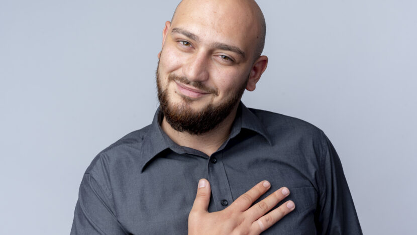 pleased young bald call center man putting hand chest looking camera isolated white background