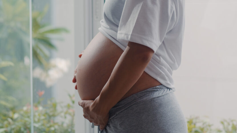 young asian pregnant woman holding her belly talking with her child mom feeling happy smiling positive peaceful while take care baby pregnancy near window living room home