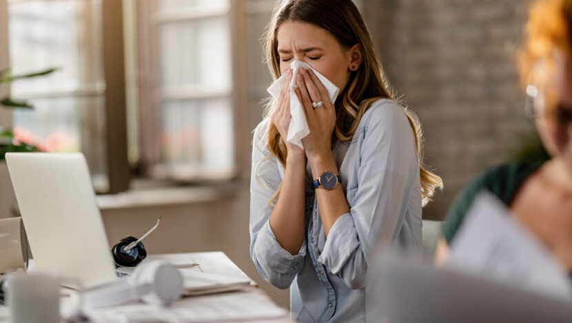 young sick businesswoman sneezing tissue while working office