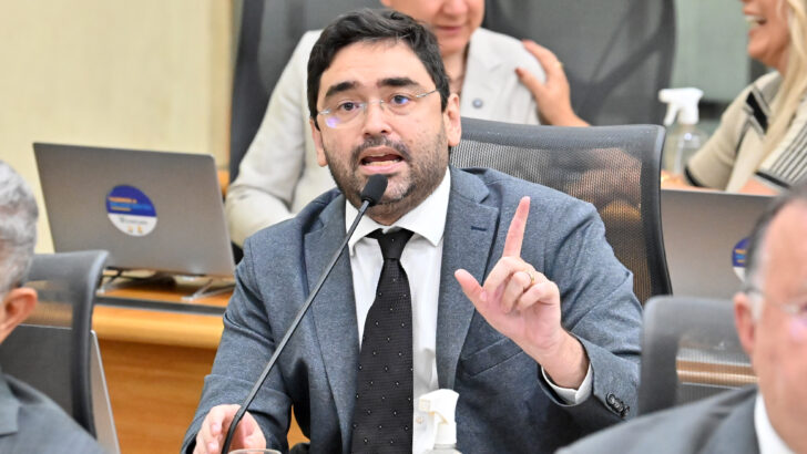 Adjuto Dias, de terno e gravata, fala ao microfone e gesticula sentado no plenário da Assembleia Legislativa
