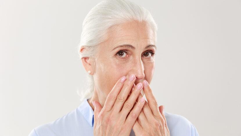 close up portrait charming old lady covering her mouth with hands Copia
