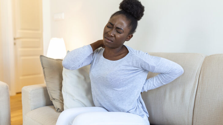 young black woman suffering from backache home portrait young girl sitting couch home with headache back pain beautiful woman having spinal kidney pain Copia