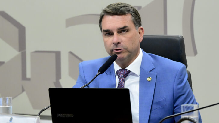 Senador Flávio Bolsonaro sentado diante de microfone durante atividade no Senado Federal