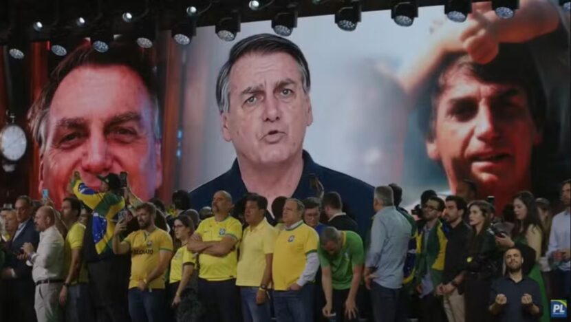 Telão exibe representação de Jair Bolsonaro durante convenção partidária, diante de participantes vestidos com as cores verde e amarela