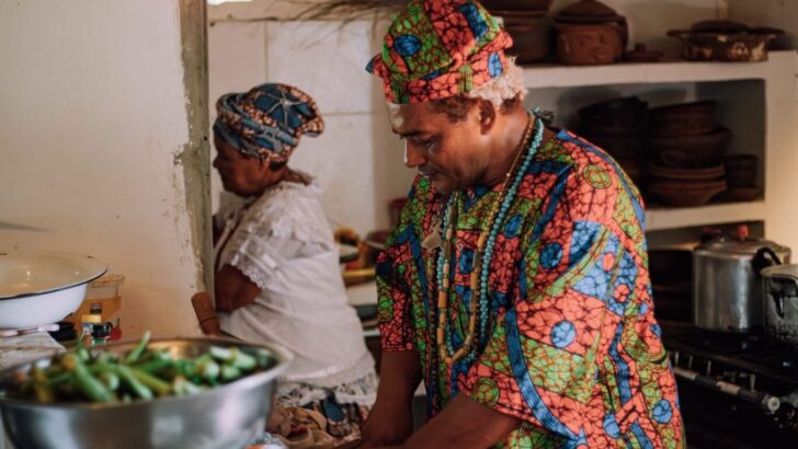 Imagem mostra um homem e uma mulher, com roupas da cultura africana, cozinhando