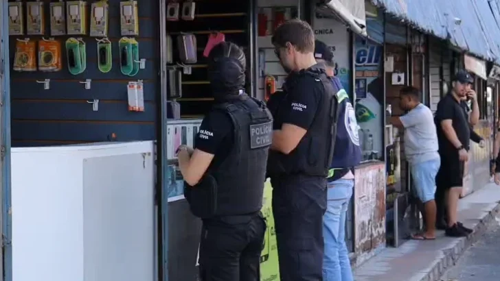 Policiais civis durante fiscalização em estabelecimento com celulares e acessórios expostos