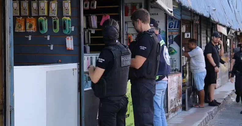 Policiais civis durante fiscalização em estabelecimento com celulares e acessórios expostos