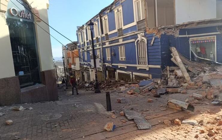 Rua coberta por escombros ao lado de prédios com paredes e estruturas danificadas