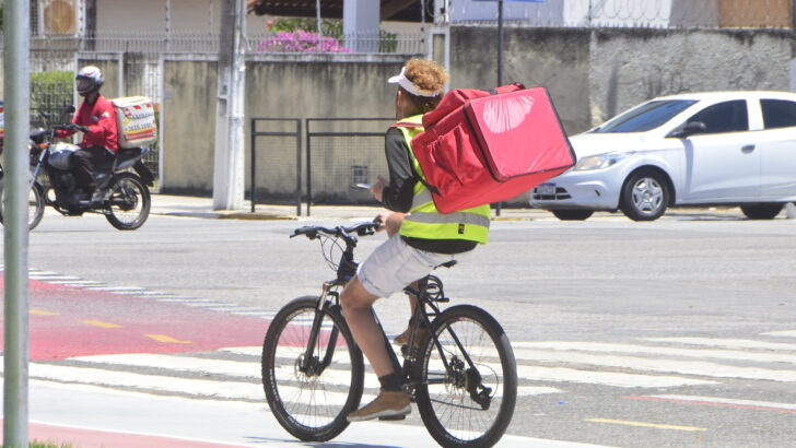 Entregador de aplicativo em bicicleta durante trabalho em via urbana