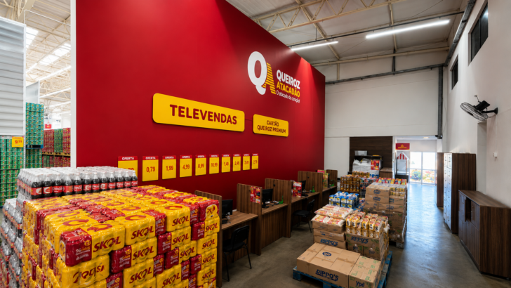 Área de televendas com balcões de atendimento, produtos empilhados e placas de ofertas dentro de uma loja do Queiroz Atacadão.