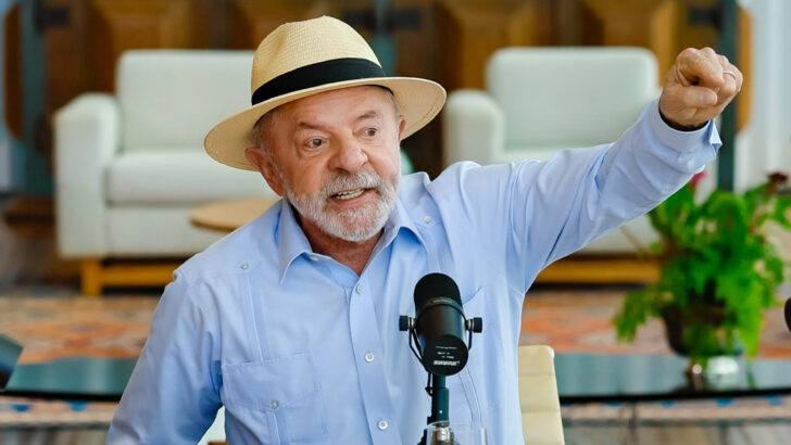 Presidente Lula, de chapéu, levanta o punho durante fala diante de um microfone