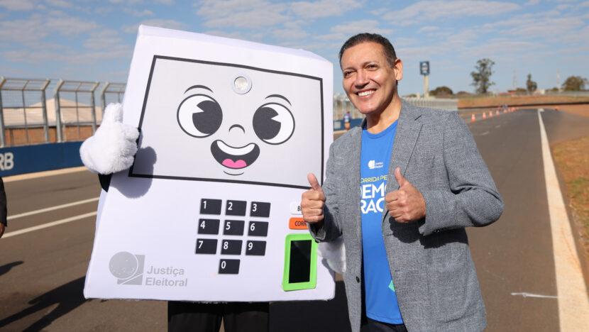 Ministro Kassio Nunes Marques posa ao lado de mascote em formato de urna eletrônica durante a Corrida Pela Democracia, em Brasília