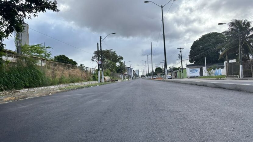 Avenida com pavimento asfaltado, canteiro central e postes de iluminação sob céu nublado