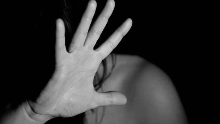 Mulher aparece com a mão aberta diante do rosto em imagem em preto e branco que representa situação de violência