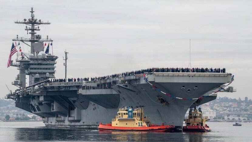 Porta-aviões USS George Washington navega acompanhado por embarcações menores, com militares reunidos no convés