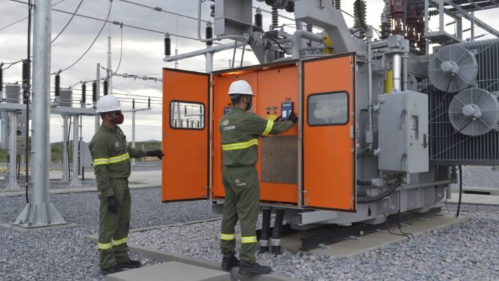 Dois profissionais trabalham em equipamentos de uma subestação de energia elétrica