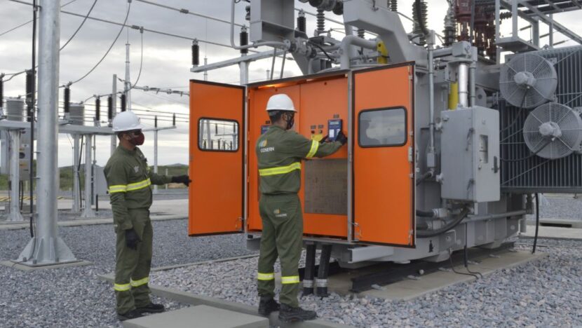 Dois profissionais trabalham em equipamentos de uma subestação de energia elétrica