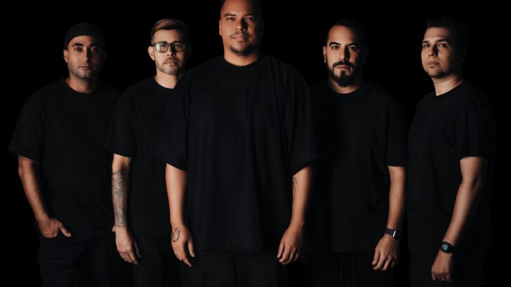 Cinco integrantes do grupo Sorriso Maroto posam para foto usando roupas pretas diante de um fundo escuro