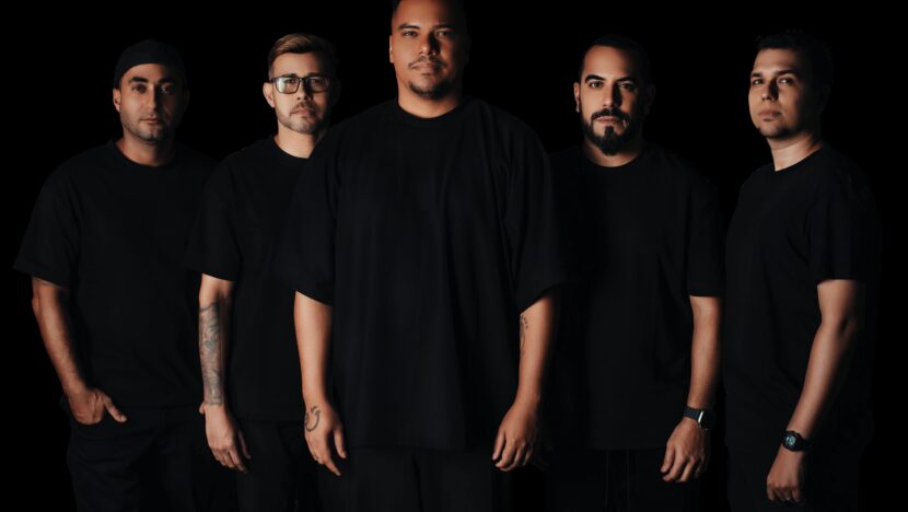 Cinco integrantes do grupo Sorriso Maroto posam para foto usando roupas pretas diante de um fundo escuro