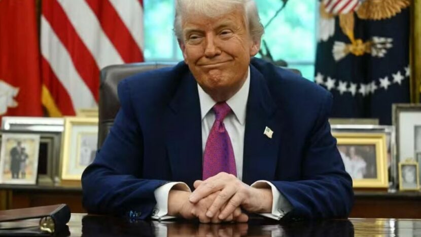 Donald Trump sentado à mesa, com bandeiras dos Estados Unidos e símbolos oficiais ao fundo