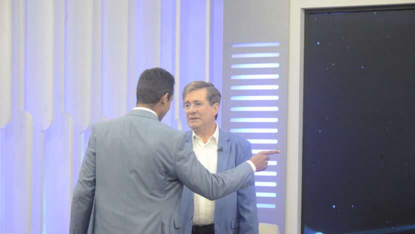 Allyson Bezerra, de costas, aponta enquanto conversa com Robério Paulino no estúdio do debate da Band RN