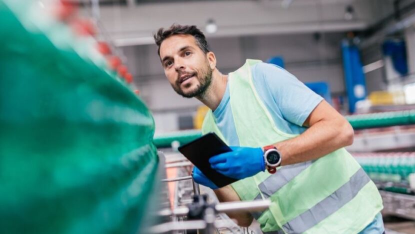 Trabalhador usa colete refletivo e luvas enquanto opera equipamento em ambiente industrial