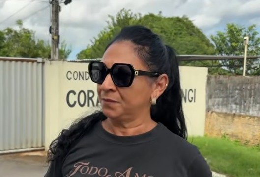 Mulher de óculos escuros concede entrevista em frente a um condomínio residencial