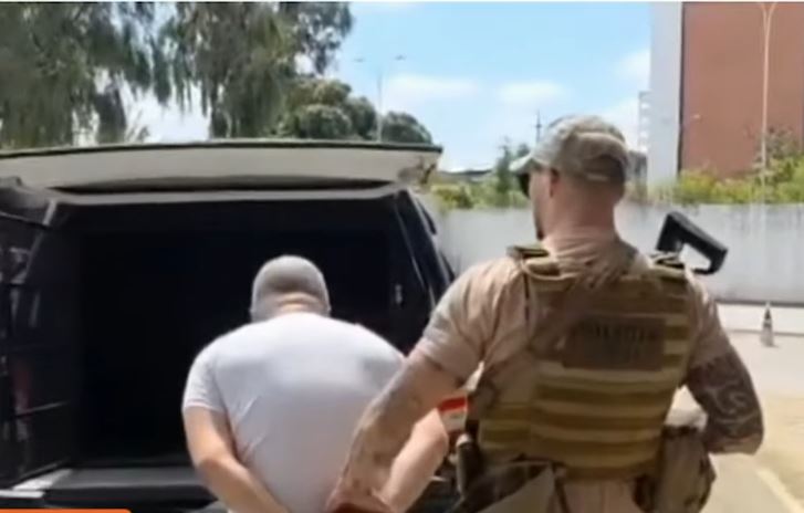 Homem com as mãos para trás é conduzido por agente de segurança em direção a um veículo
