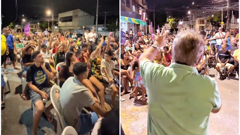 Público acompanha evento realizado à noite em uma rua, enquanto um homem fala diante das pessoas reunidas em cadeiras