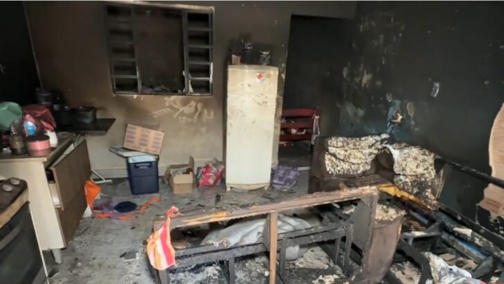 Interior de residência com paredes, móveis e objetos danificados pelo fogo após incêndio