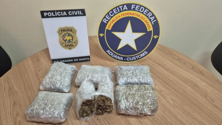 Pacotes com material apreendido sobre mesa ao lado de identificações da Polícia Civil do Rio Grande do Norte e da Receita Federal