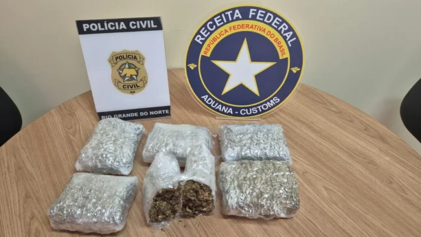 Pacotes com material apreendido sobre mesa ao lado de identificações da Polícia Civil do Rio Grande do Norte e da Receita Federal