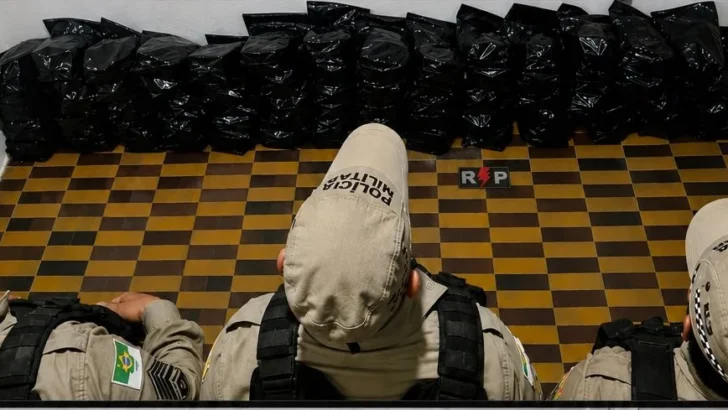 Policiais militares diante de diversos pacotes pretos apreendidos durante ocorrência em Canguaretama