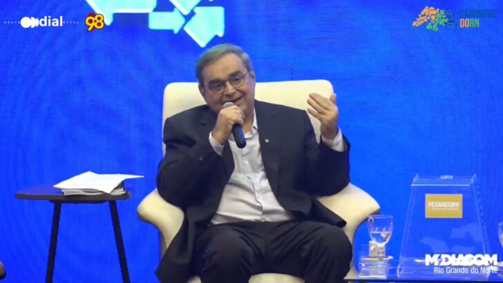 Álvaro Dias sentado em uma poltrona, segurando um microfone e gesticulando durante a sabatina do Fórum Caminhos do RN