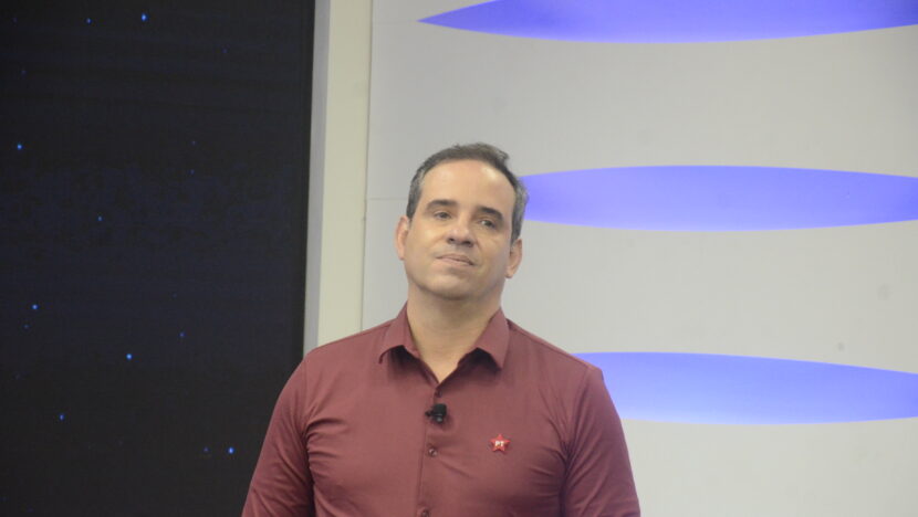 Cadu Xavier usa camisa vinho com símbolo do PT durante participação em estúdio de televisão