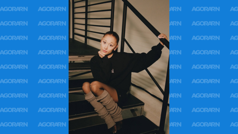 Ariana Grande posa sentada em uma escada, usando moletom preto e polainas cinzas
