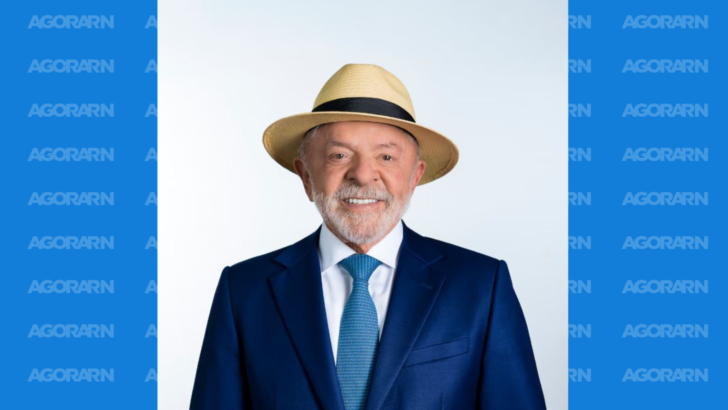 Luiz Inácio Lula da Silva aparece de terno azul, gravata e chapéu panamá diante de fundo claro
