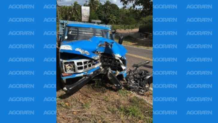 Caminhão azul com a parte dianteira danificada e motocicleta destruída após colisão em uma rodovia