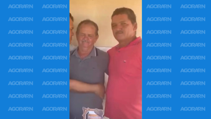 Dois homens aparecem lado a lado, um vestindo camisa cinza e outro camisa vermelha