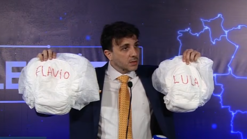 Renan Santos exibiu fraldas com os nomes de Lula e Flávio Bolsonaro antes do primeiro debate presidencial promovido pela Band. - Foto: Reprodução Youtube Band Jornalismo