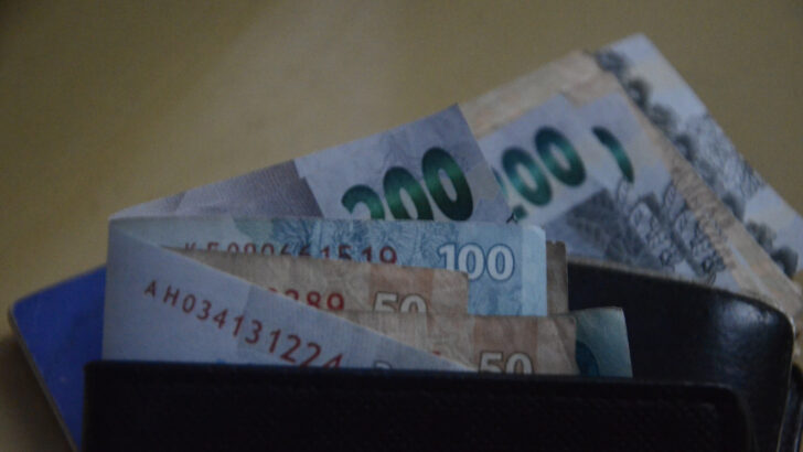 Cédulas de real de 200, 100 e 50 saindo de uma carteira de couro.