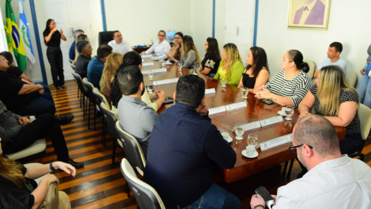 Grupo reunido ao redor de uma mesa em sala do Palácio da Resistência, com uma intérprete de Libras em pé ao fundo