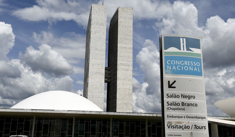 Fachada do Congresso Nacional, em Brasília, com as duas torres, uma das cúpulas e uma placa de orientação para visitantes