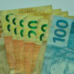 Cédulas de dinheiro brasileiro de diferentes valores estão sobrepostas e espalhadas sobre uma superfície clara.
