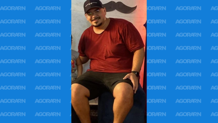 Wesley Souza sorri usando boné preto, óculos e camiseta vermelha diante de uma parede decorada