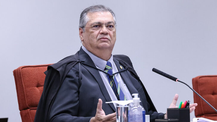 Flávio Dino sentado na bancada do Supremo Tribunal Federal, usando toga e diante de um microfone