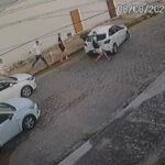Homens descem de três carros brancos e correm por uma rua de paralelepípedos registrada por uma câmera de segurança